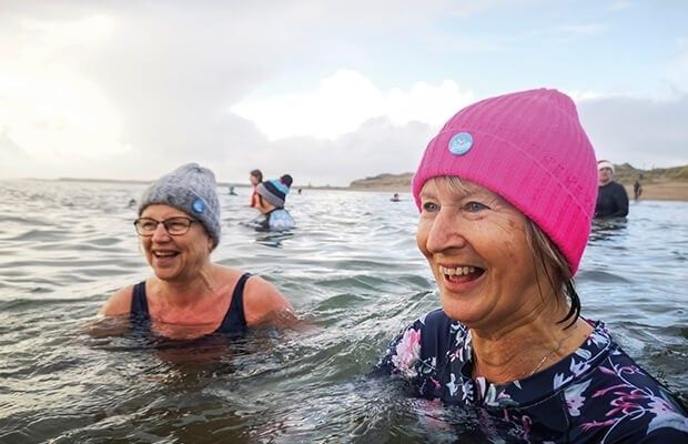 Deux nageuses rient dans la mer froide, coiffées de bonnets